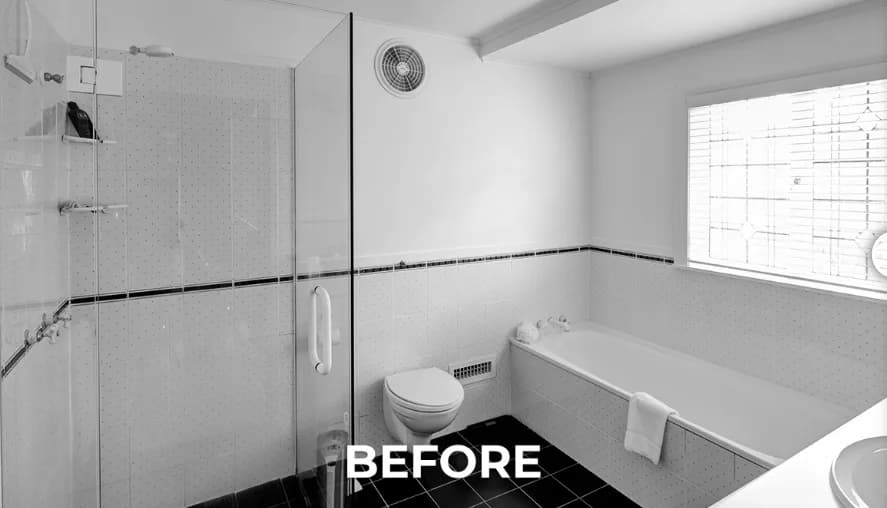 Black-and-white photograph of the bathroom before renovation, showing small dotted-pattern wall tiles with a black trim border, black floor tiles, a glass shower screen, and a wall-hung toilet.