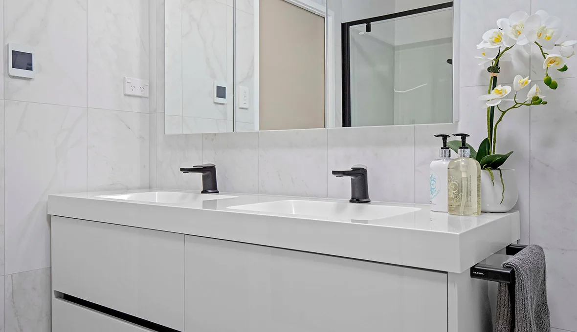 Double vanity with two rectangular basins on a white stone top, matte black wall-mounted mixers, a wide mirrored cabinet, and full-height white marble-look wall tiles.