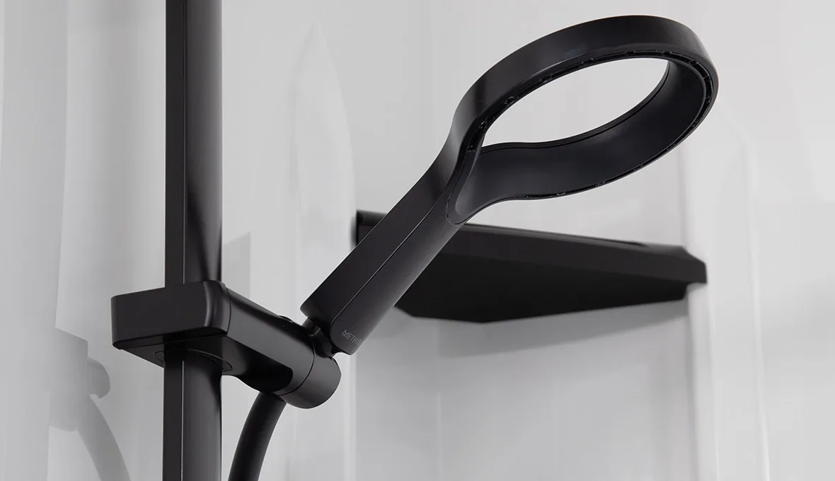 Close-up of a matte black loop-handle handheld shower head on a rail, mounted on a frameless glass shower screen.