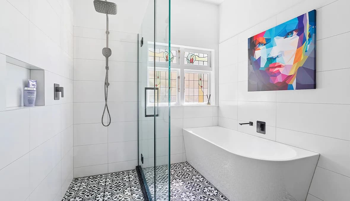 White freestanding bath with a matte black wall-mounted spout, a colourful portrait artwork above, a round white vessel basin on a black wall-hung vanity, and a black timber sliding barn door, all on black-and-white patterned floor tiles.