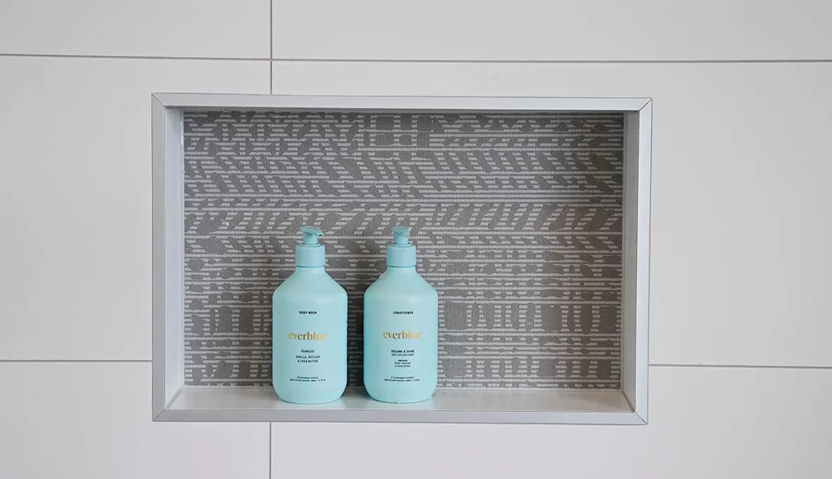 Recessed tiled shower niche with a patterned grey feature tile, holding two turquoise pump-bottle toiletries.